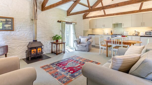A cozy living room with a stone wall, a fireplace, a dining area, and a kitchen. - 2 Bed in Launceston (oc-d31000) (Trevadlock)