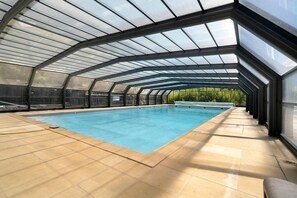 An indoor swimming pool with a glass ceiling, surrounded by a tiled floor. - Holiday Home “Maison 4 Personnes” with Optional AC and Shared Pool (Calviac-en-Périgord)