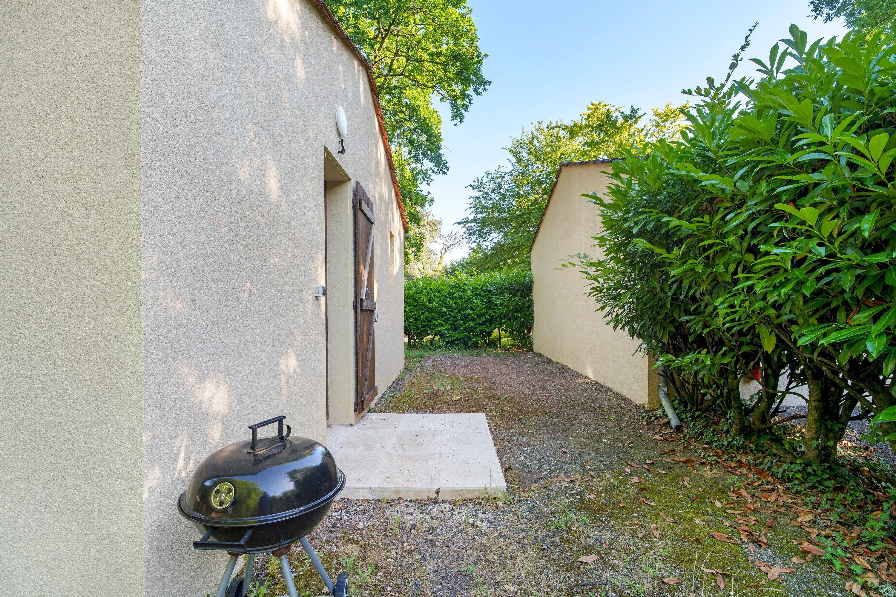 Een smal buitenterreinpad dat leidt naar een gebouw met een barbecue en een deur.