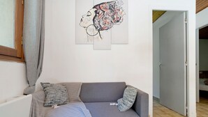 Ein graues Sofa mit gemusterten Kissen, ein abstraktes Wandbild und eine Holzbalkendecke.