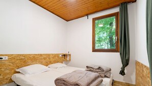 Ein Schlafzimmer mit einem Holz-Kopfteil, einem Fenster mit Blick auf Bäume und einem Bett mit einer gefalteten Decke.