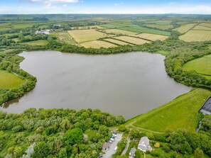 An aerial view of a lake surrounded by green fields and a few buildings. - 1 Bed in Kilkhampton (oc-j31131) (Pancrasweek)