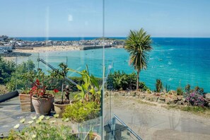 Ein Küstenblick mit Balkon und Meerblick, Kübelpflanzen und einer Palme.