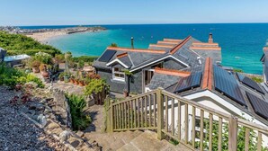 A coastal property with a staircase leading to a house with solar panels, a garden, and a view of the beach and sea. - 3 Bed in St. Ives (oc-sims01) (Carbis Bay)