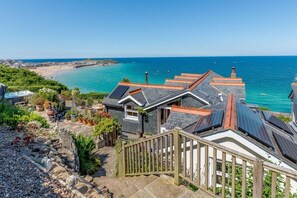 Ein Küsteneigentum mit einer Treppe, die zu einem Haus mit Solaranlage, Garten und Blick auf Strand und Meer führt.