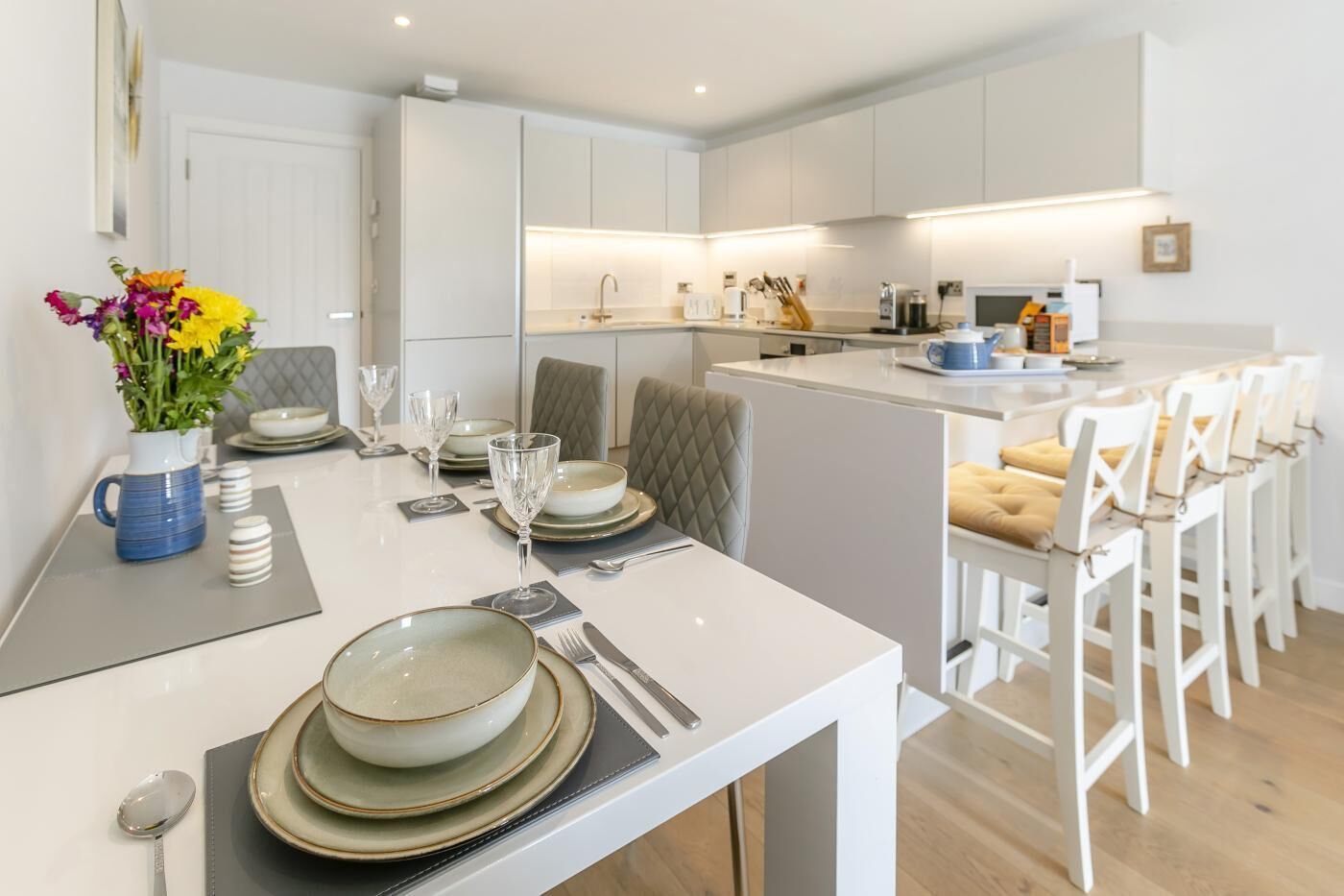 A modern kitchen with white cabinetry, a central island, and a dining area with white chairs and a table set for six.