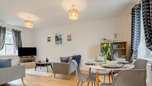 Una sala de estar moderna con televisor, sofá, mesa de comedor y sillas.