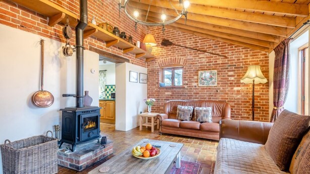 A cozy living room with a brick fireplace, a sofa, a coffee table with fruit, and a wicker basket. - 6 Bed in Wangford (oc-e31107) (Wangford)