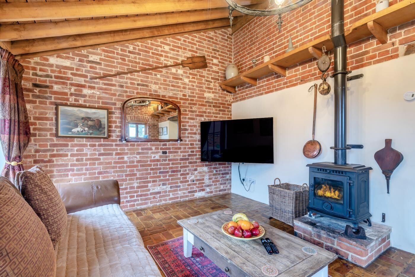A living room with a brick wall, a television, a fireplace, a sofa, and a coffee table with fruit.