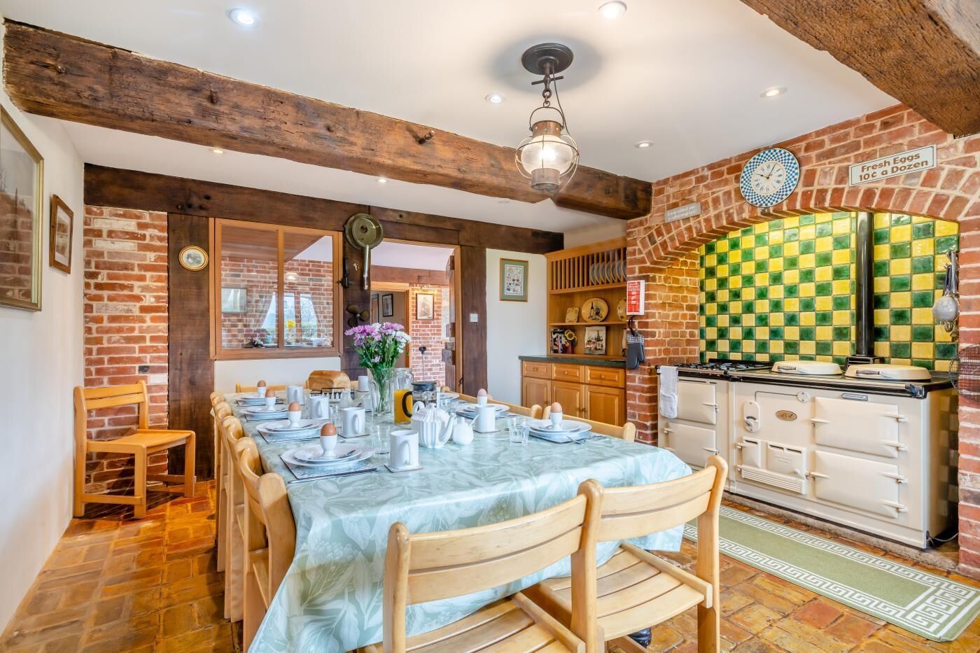Uma sala de jantar com uma mesa comprida posta para refeição, uma parede de tijolos e um fogão antigo.