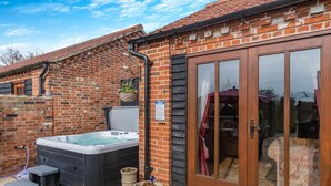 A brick house with a hot tub, a sliding glass door, and a small outdoor seating area. - 6 Bed in Wangford (oc-e31107) (Wangford)