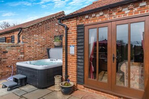 A brick house with a hot tub, a sliding glass door, and a small outdoor seating area. - 6 Bed in Wangford (oc-e31107) (Wangford)