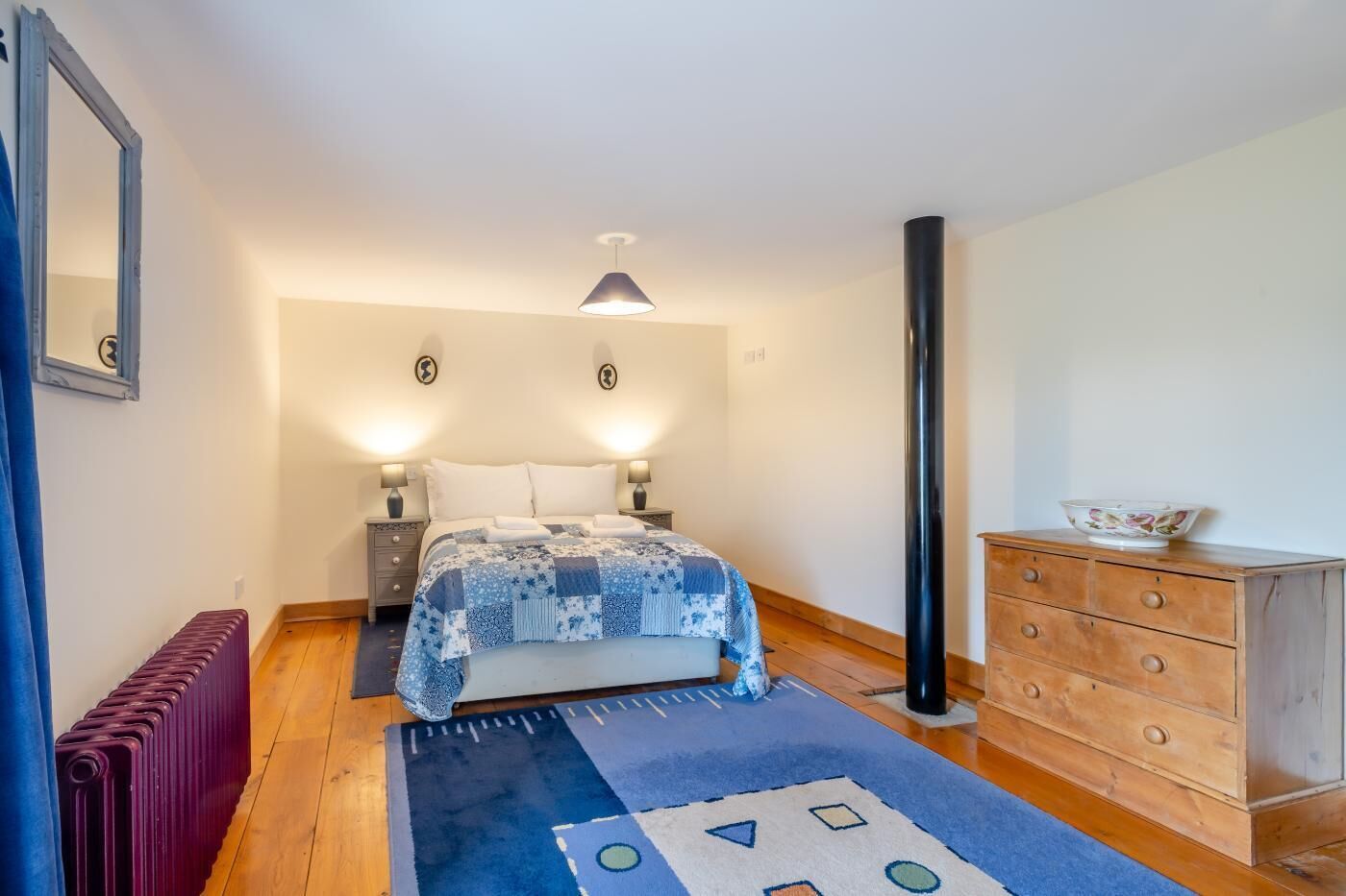 A bedroom with a bed, bedside lamps, a dresser, a radiator, and a rug.