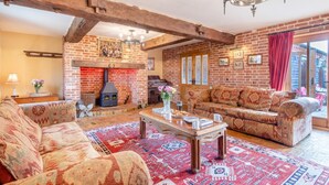 A cozy living room with a brick fireplace, patterned sofas, and a wooden coffee table. - 6 Bed in Wangford (oc-e31107) (Wangford)