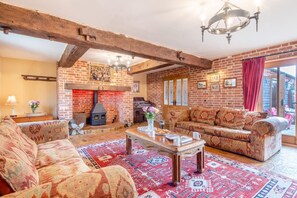 A cozy living room with a brick fireplace, patterned sofas, and a wooden coffee table. - 6 Bed in Wangford (oc-e31107) (Wangford)