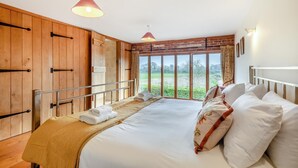 A bedroom with a large bed, wooden panel walls, a window with a view of greenery, and two pendant lights. - 6 Bed in Wangford (oc-e31107) (Wangford)