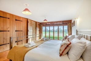 A bedroom with a large bed, wooden panel walls, a window with a view of greenery, and two pendant lights. - 6 Bed in Wangford (oc-e31107) (Wangford)