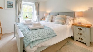 Un dormitorio ordenado con cama, mesitas de noche y una ventana con cortinas.