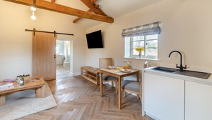 A cozy kitchen with wooden beams, a dining table with chairs, a TV mounted on the wall, and a window with a view. - 1 Bed in Leeds (oc-b31067) (Leeds)
