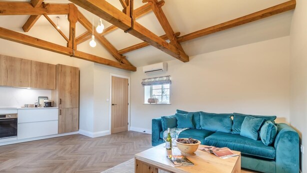 A spacious living area with a wooden ceiling, a teal sofa, a wooden coffee table, and a kitchen in the background. - 1 Bed in Leeds (oc-b31067) (Leeds)