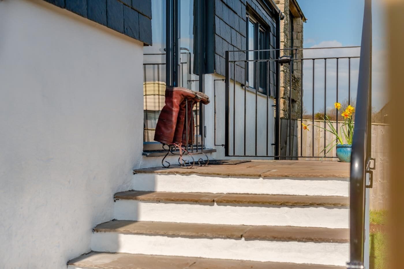 Un conjunto de escalones exteriores que conducen a un edificio con una reja de metal y una maceta con flores amarillas.