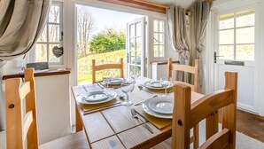 A dining area with a table set for four, wooden chairs, and a view of the outdoors through open doors. - 2 Bed in Duloe (oc-f31903) (Duloe)