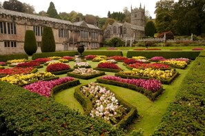 Un jardin à la française, avec des parterres de fleurs disposés selon des motifs géométriques, et un bâtiment historique en arrière-plan.