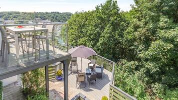 A rooftop terrace with outdoor furniture, a glass balustrade, and a view of a forested area.