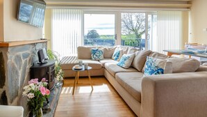 Ein Wohnzimmer mit Kamin aus Stein, einem beigen Sofa und einem Essbereich mit Glastisch.