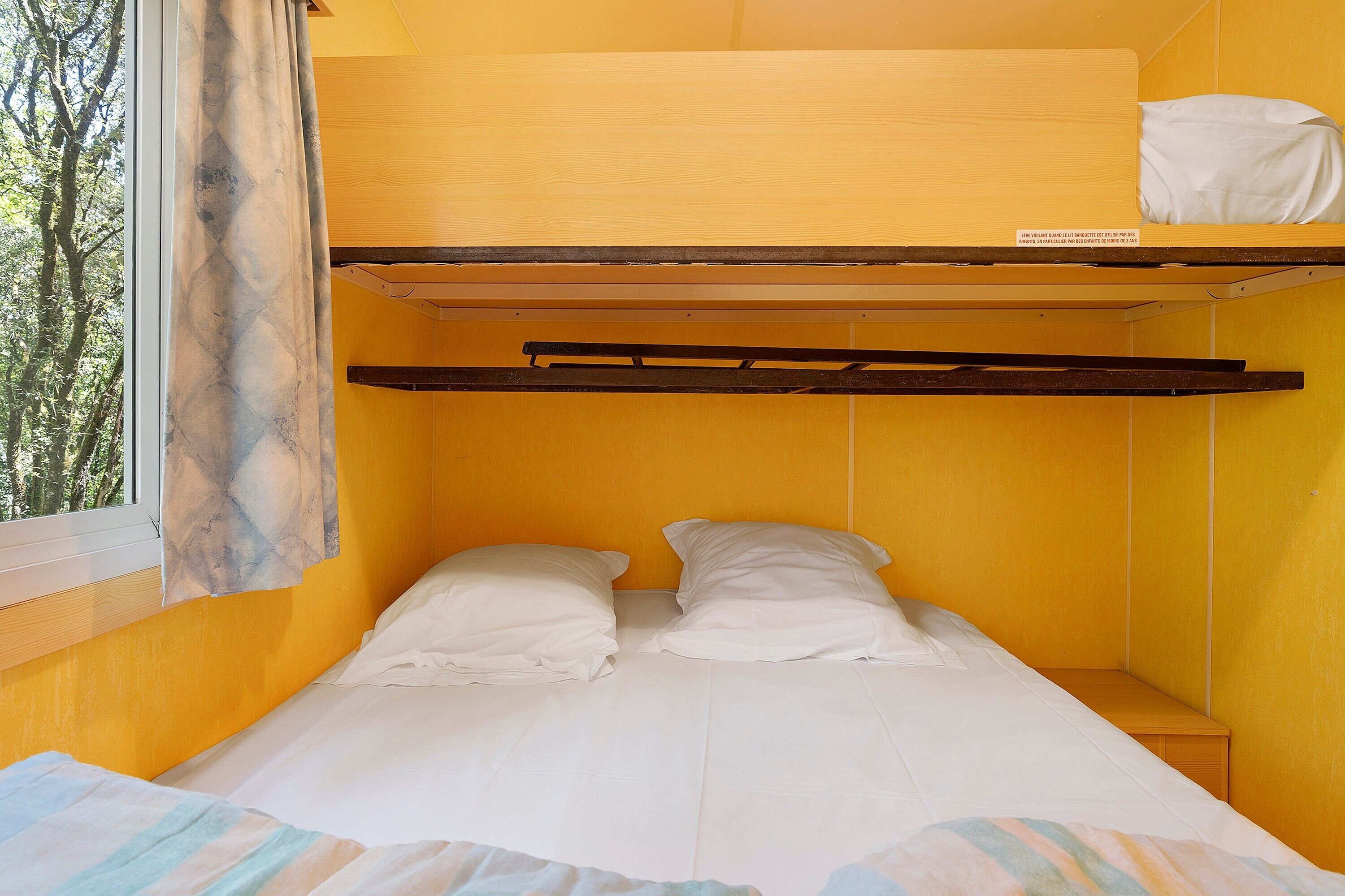Een slaapkamer met een stapelbed, raam, gordijnen en een houten hoofdbord.