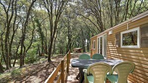 Une terrasse en bois avec une table et des chaises, entourée d’arbres.