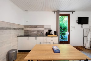 Une cuisine moderne avec une table en bois, une poubelle et un téléviseur fixé au mur.