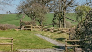 Un paisaje rural con un camino de grava que lleva a un portón de madera.