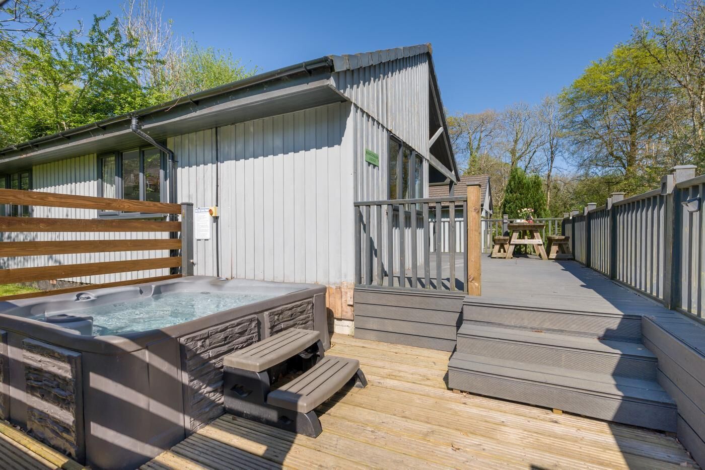 A hot tub with a wooden deck, a metal fence, and a wooden bench.