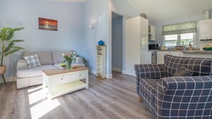 Uma sala de estar moderna com sofá, mesa de centro e área de jantar, com cozinha ao fundo.