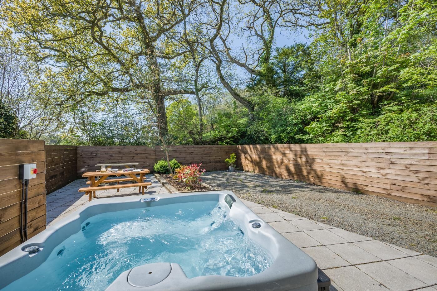 A hot tub in a backyard with a wooden fence, a picnic table, and a garden area.