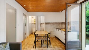 Uma cozinha moderna com teto de madeira, área de jantar com mesa e cadeiras, e uma porta de vidro deslizante que dá para um jardim.