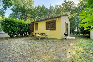 Ein kleines, gelbes Gebäude mit einem Picknicktisch und einem Grill im Garten.