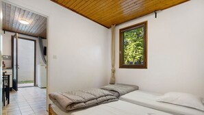 Quarto com duas camas, janela com vista para o verde, teto de madeira e porta que dá para uma área externa.