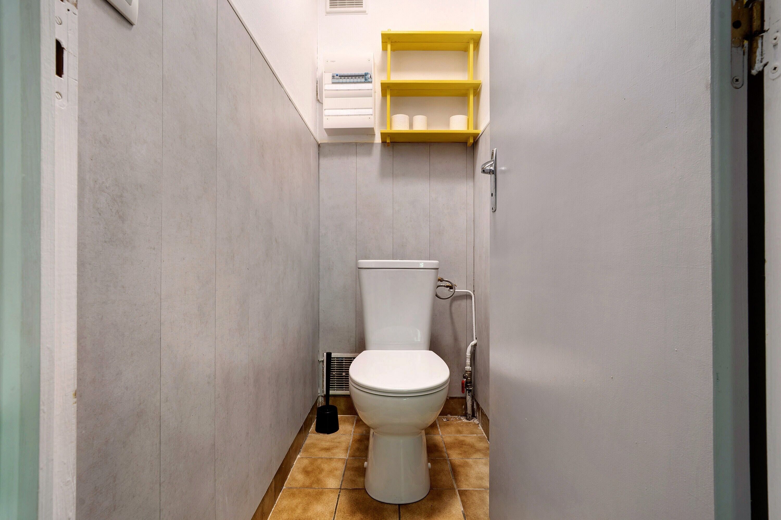 Un baño pequeño con inodoro, un estante con artículos de aseo y una rejilla en la pared.