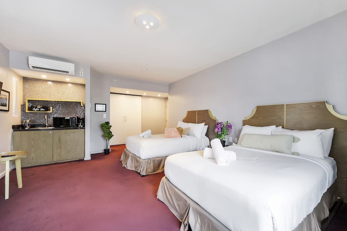 A hotel room with two beds, a kitchenette, and a small table.