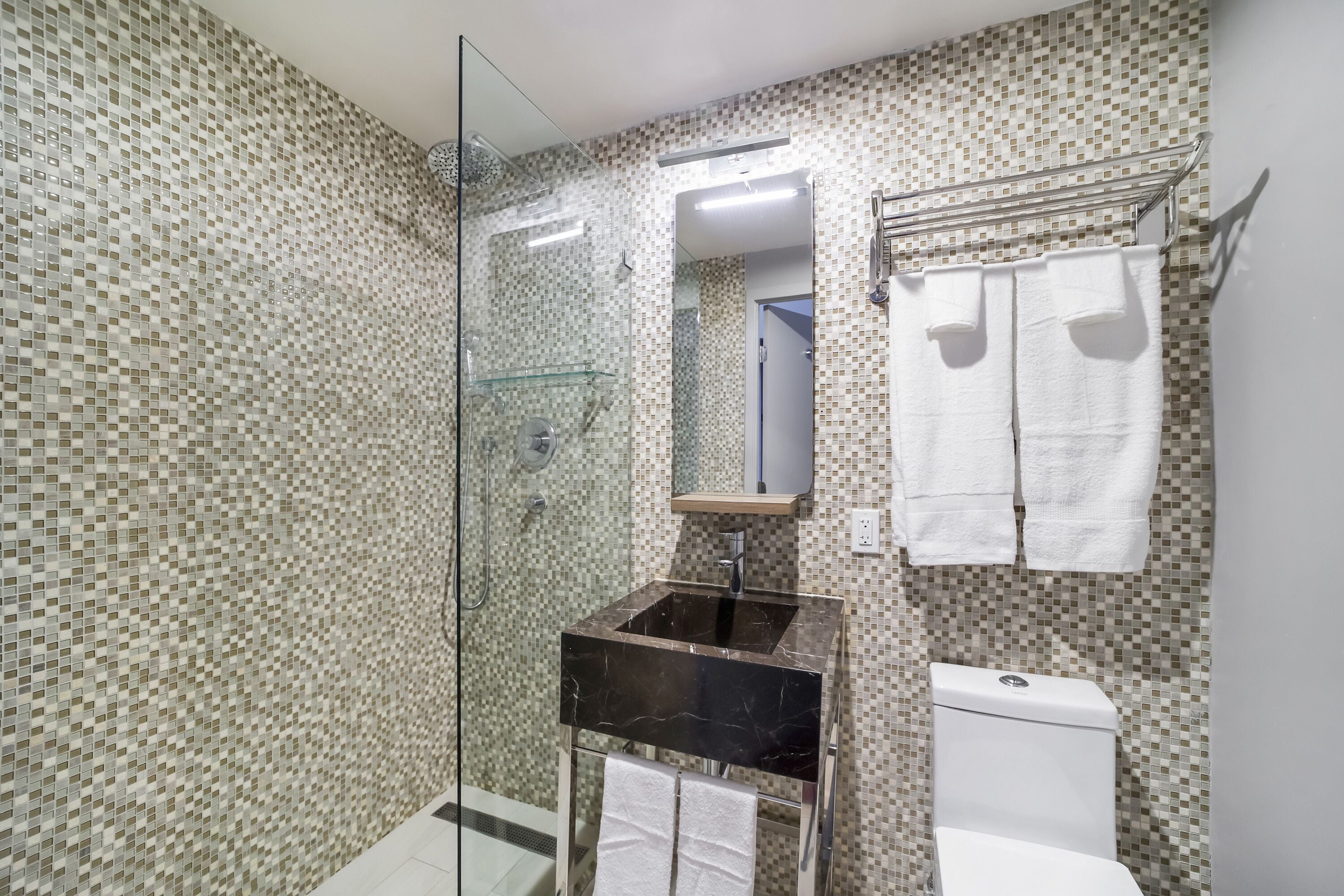 A bathroom with mosaic tile walls, a glass shower enclosure, a black sink, and a white toilet.