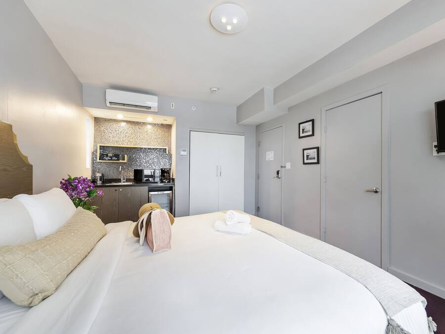 A hotel room with a bed, a kitchenette, a TV, and a door.