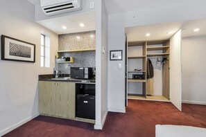 A modern kitchen with a dishwasher, microwave, and coffee machine, a closet with hanging clothes, and a framed picture on the wall. - Alamo Hotel (Miami Beach)
