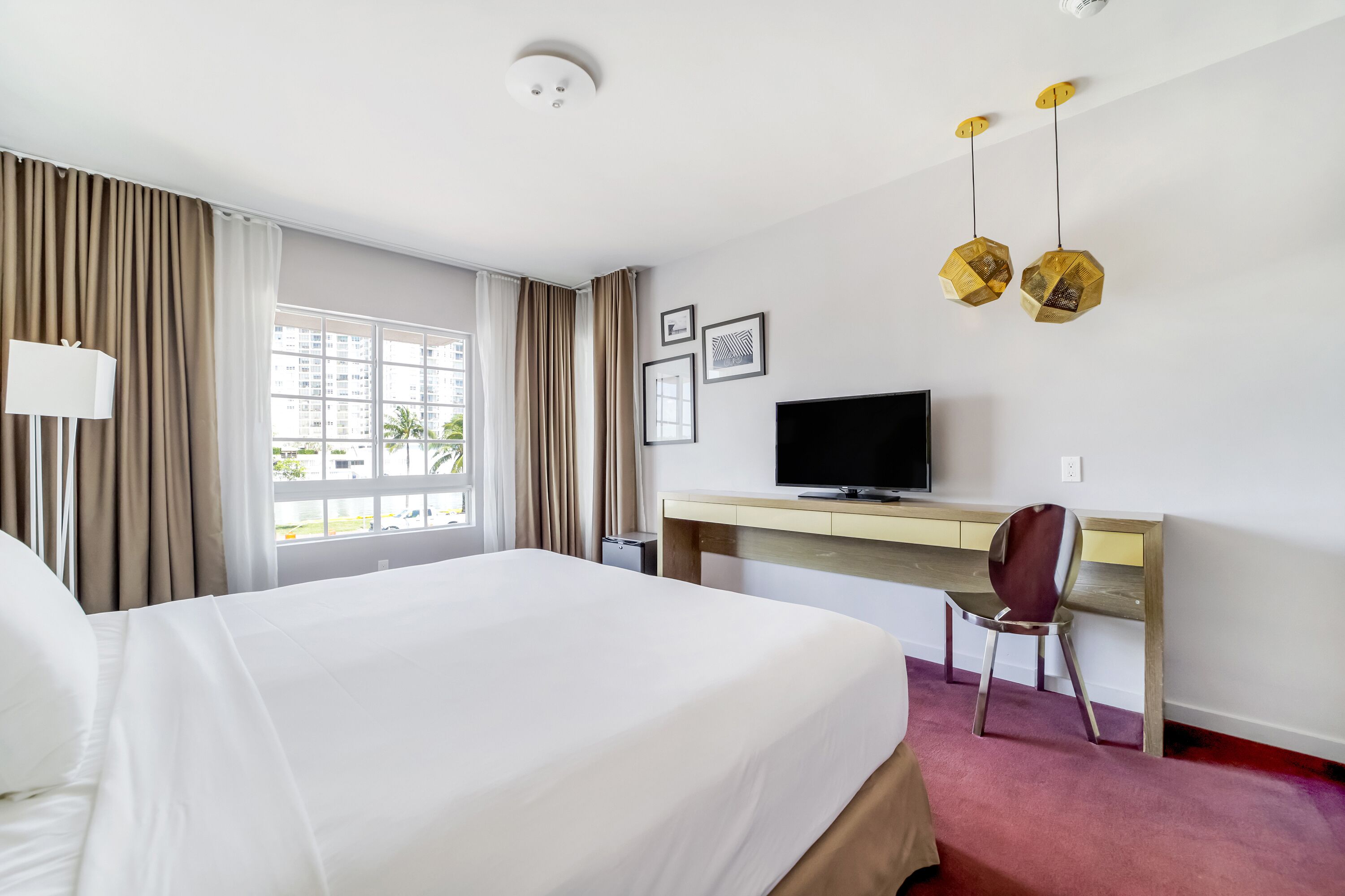 A hotel room with a large bed, a desk with a computer, a chair, and a TV.