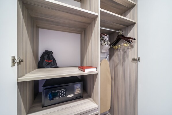 A hotel room with a built-in safe, a red book on a shelf, and a hanging coat rack. - Alamo Hotel (Miami Beach)