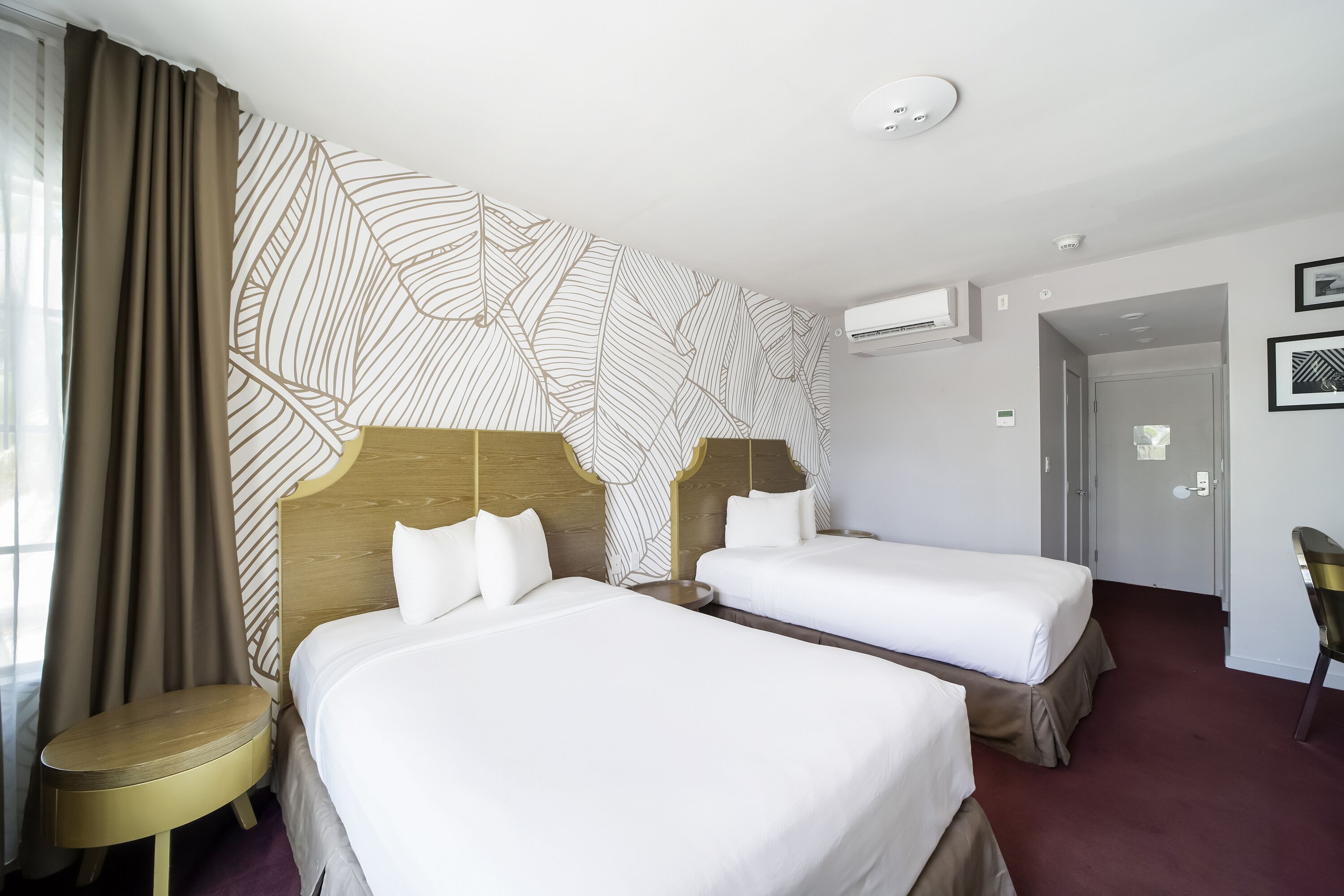 A hotel room with two beds, a round table, and a large window with curtains.