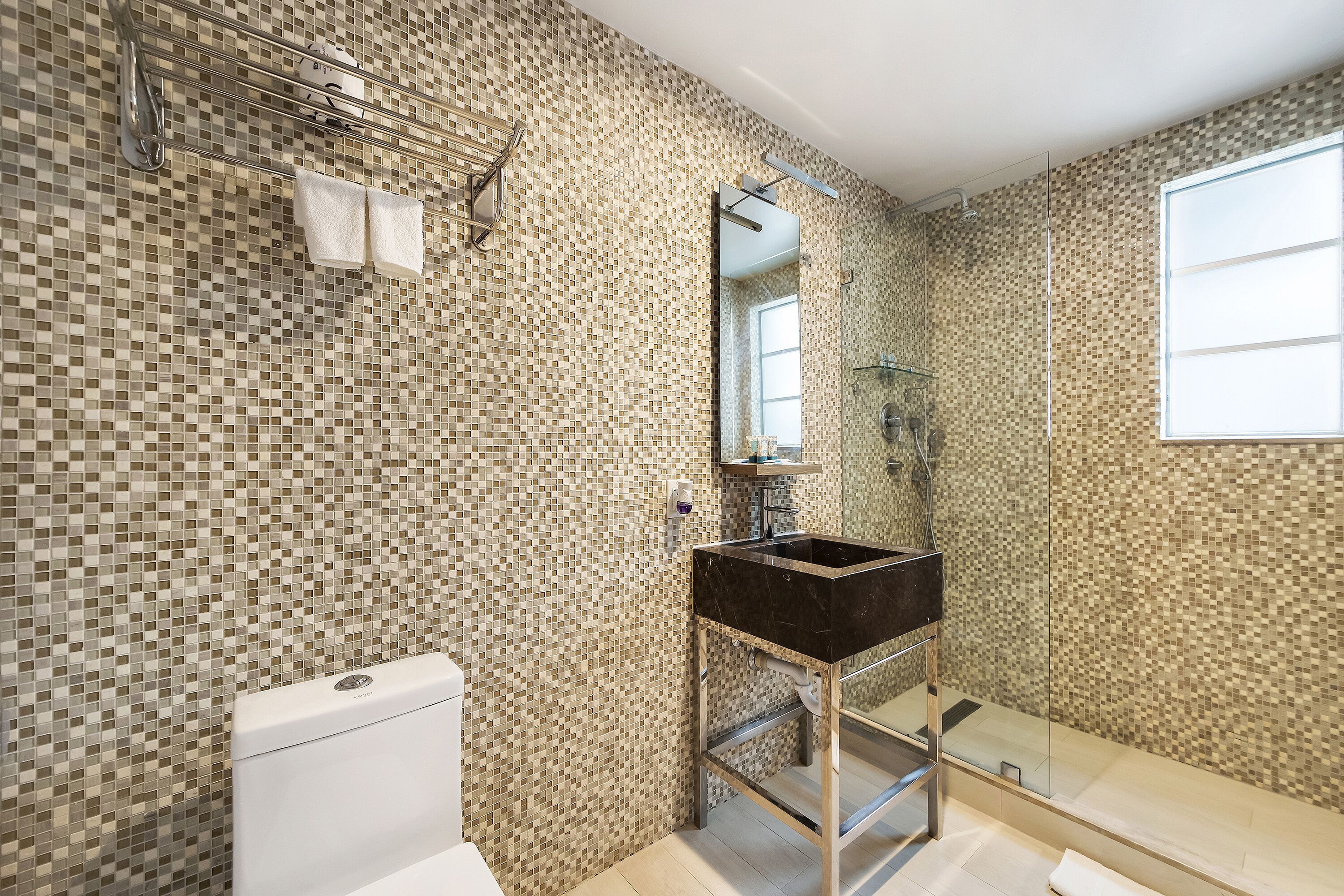 A bathroom with mosaic tile walls, a white toilet, a black sink, and a glass shower enclosure.