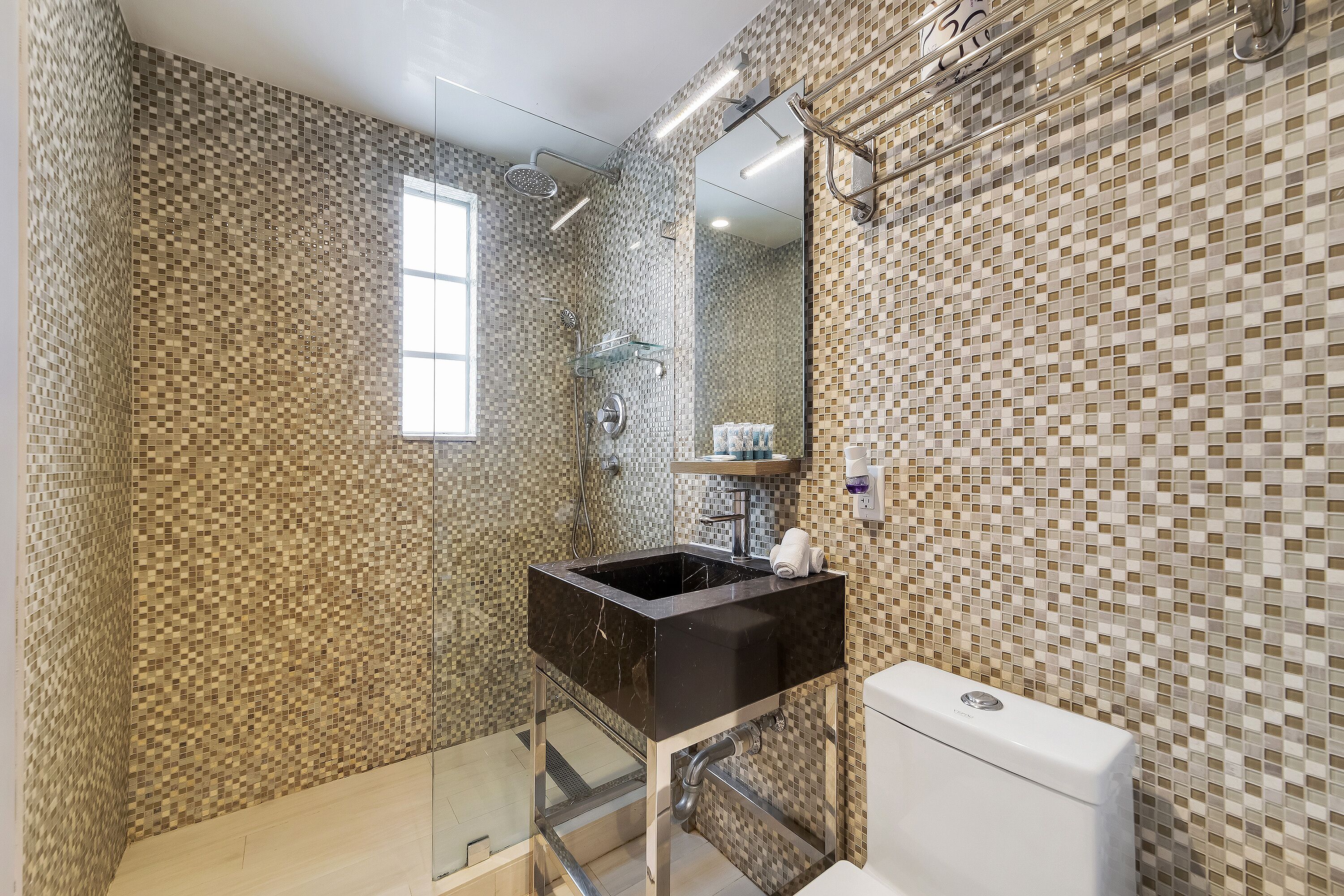 A bathroom with mosaic tile walls, a glass shower enclosure, a black sink, and a white toilet.