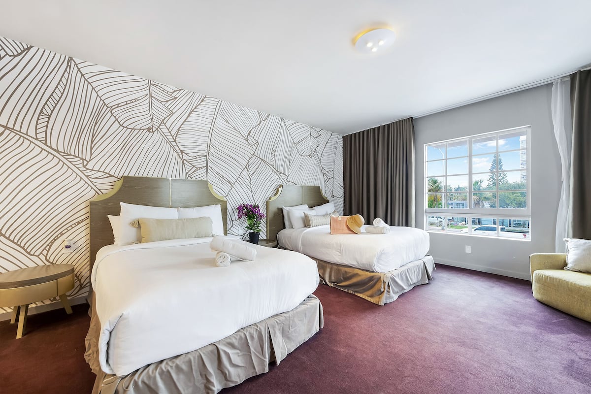 A hotel room with two beds, a large window, and a patterned wall.